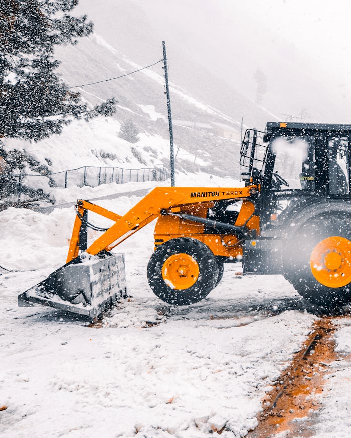 Yellow loader clearing snow on a winter day in a snowy landscape.